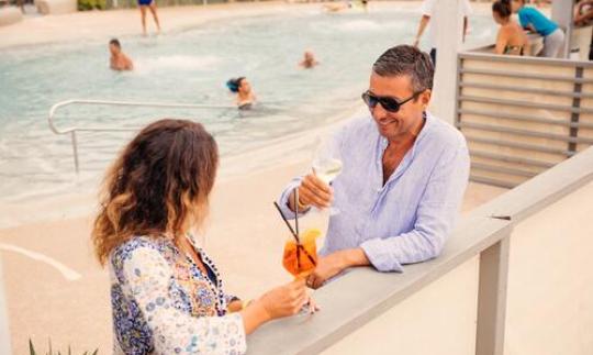 Coppia sorride e brinda a bordo piscina, atmosfera rilassata e gioiosa.
