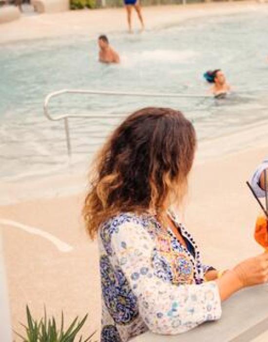 Coppia sorride e brinda a bordo piscina, atmosfera rilassata e gioiosa.